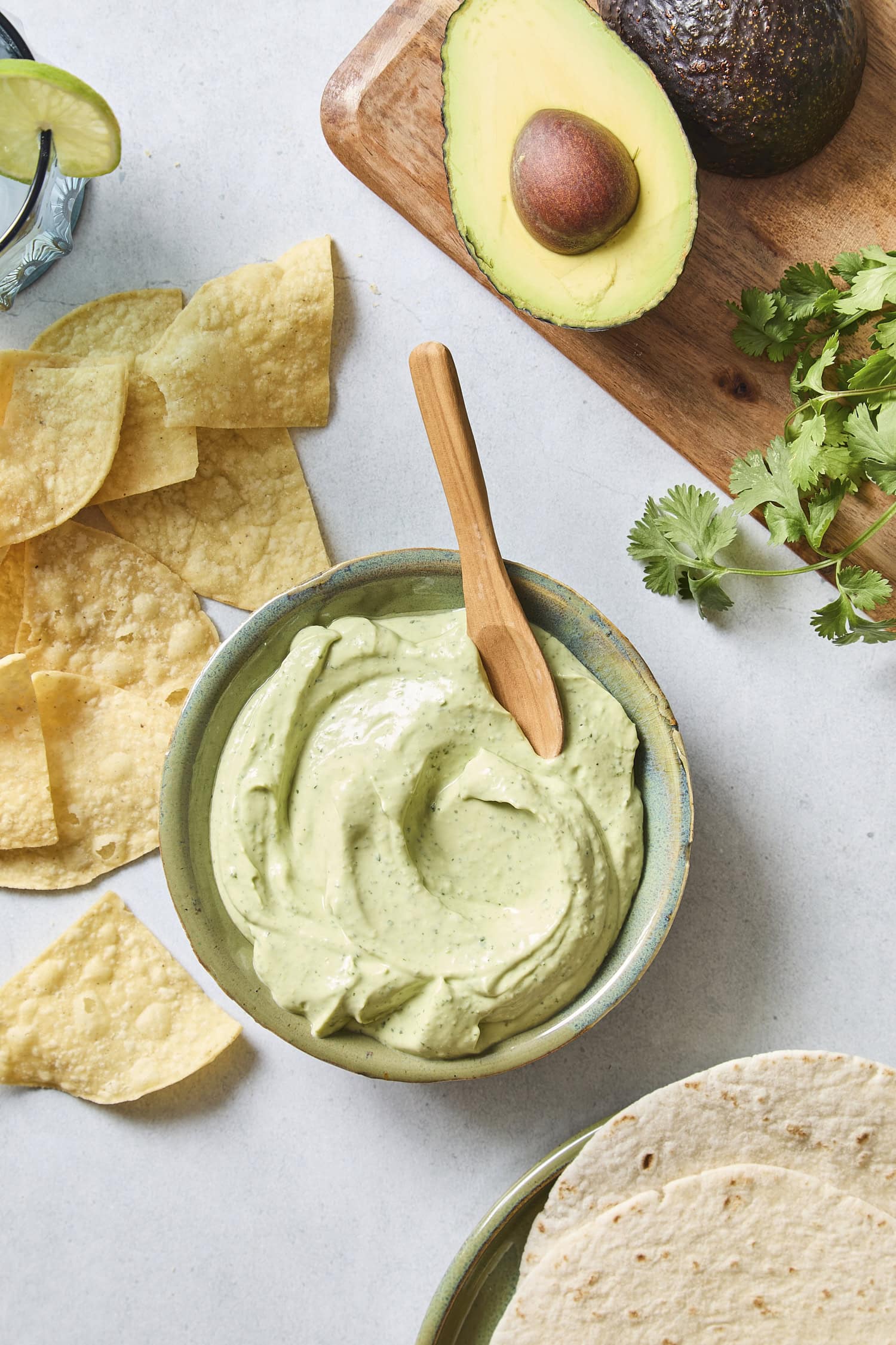 Bowl with swirled green avocado sauce with wooden spoon scooping.