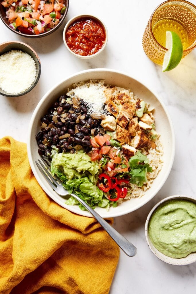 White bowl with chicken, black beans, rice, and toppings.