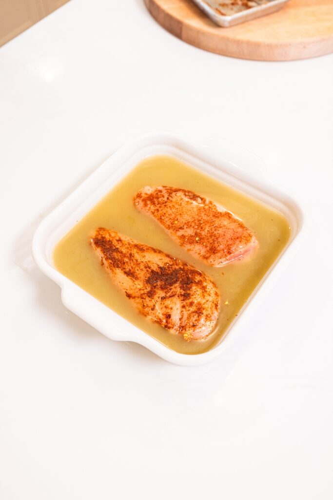 Raw chicken seasoned with taco seasoning in white baking dish with liquid.