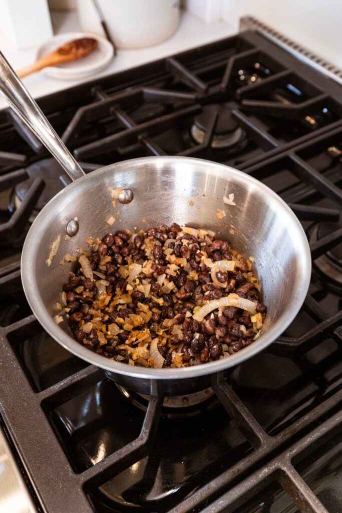 Black beans and onion in pan on stovetop.