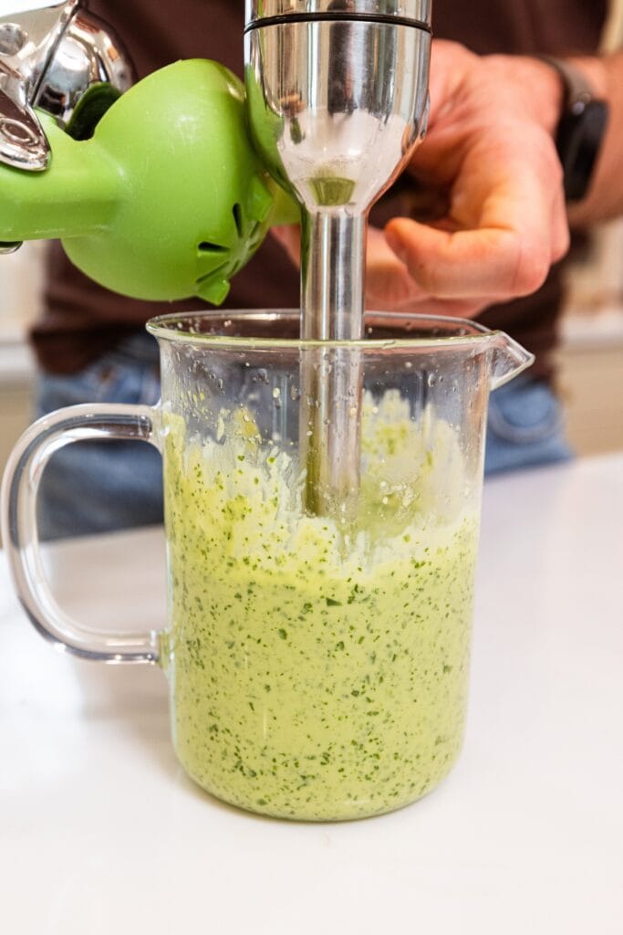 Immersion blender mixing together green colored dressing for chicken rice bowls.