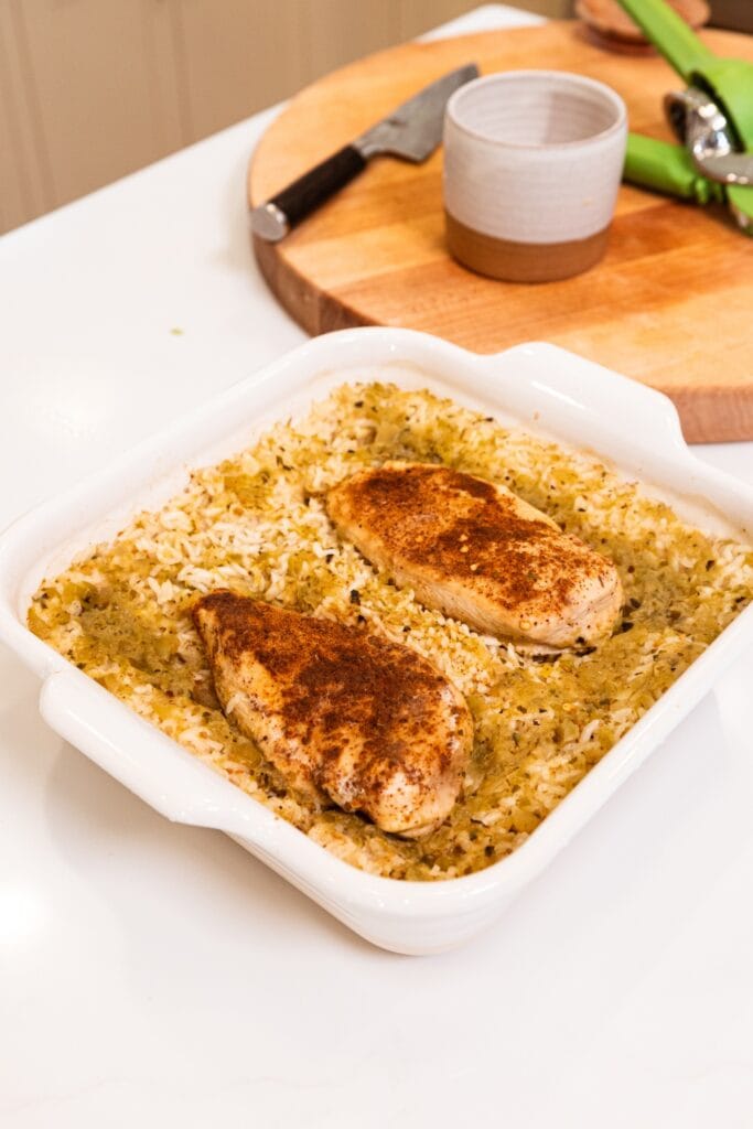 Chicken in white baking dish on top of rice after cooking.