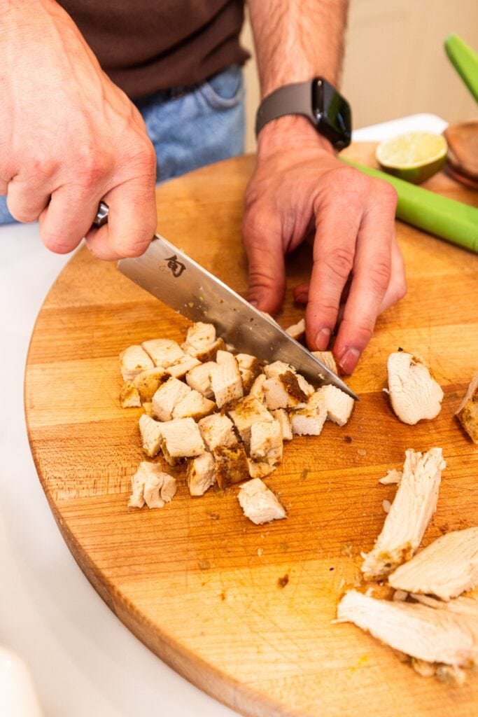 Knife chopping up chicken into bite-size pieces for chicken rice bowls.