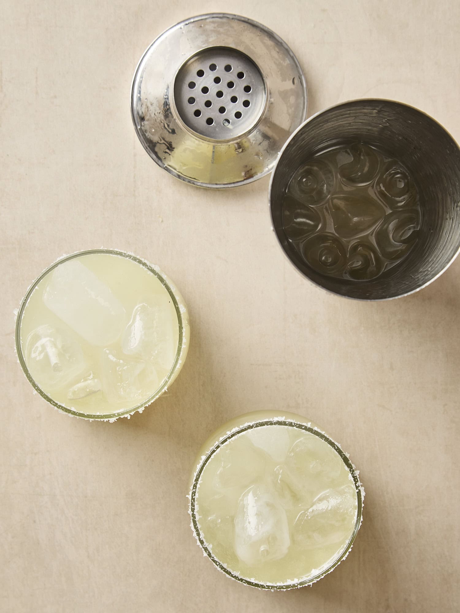 Two cocktail glasses filled with margarita with shaker open to the side.