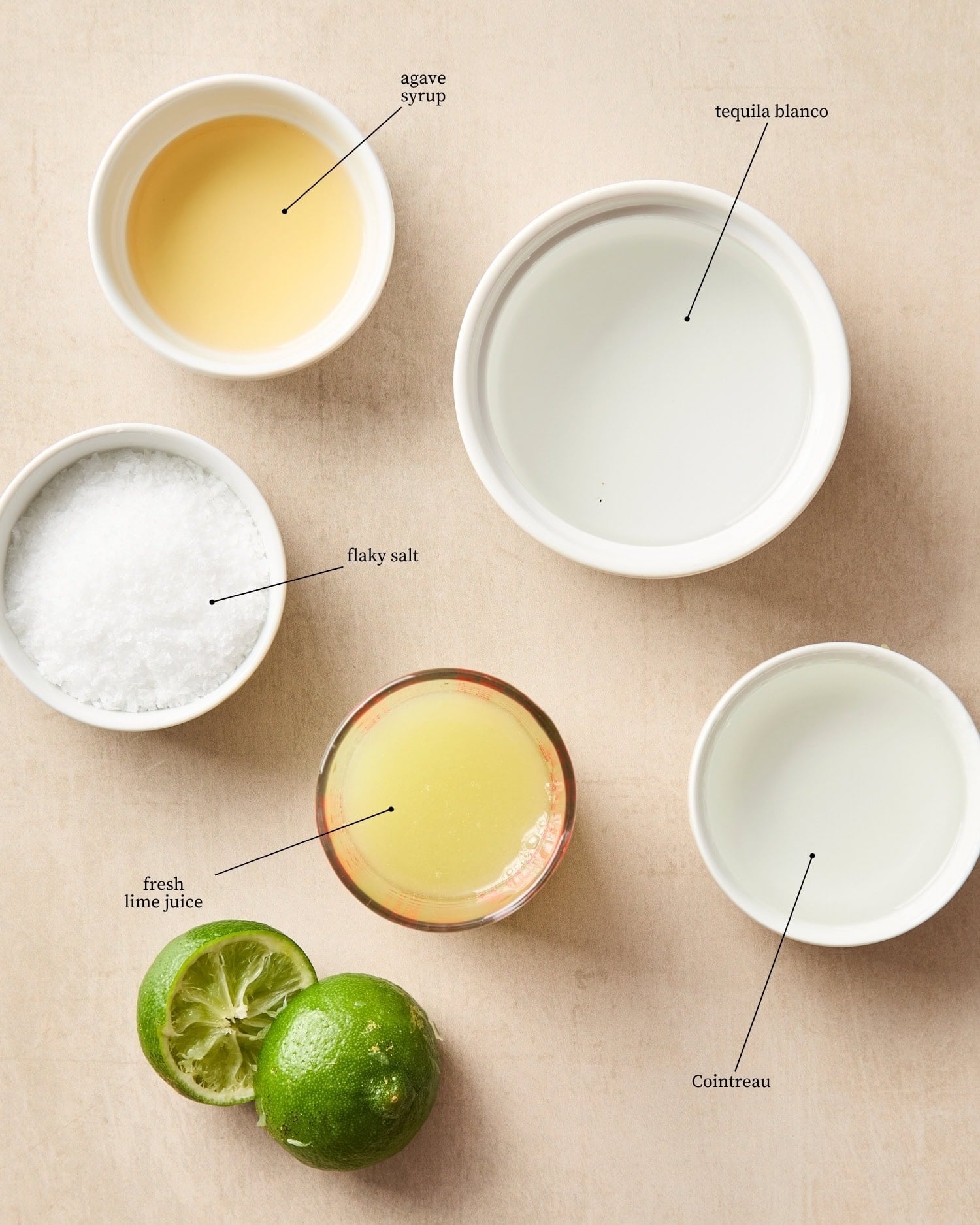 Surface filled with ingredients needed for a classic margarita recipe including tequila, Cointreau, agave syrup, and lime juice.