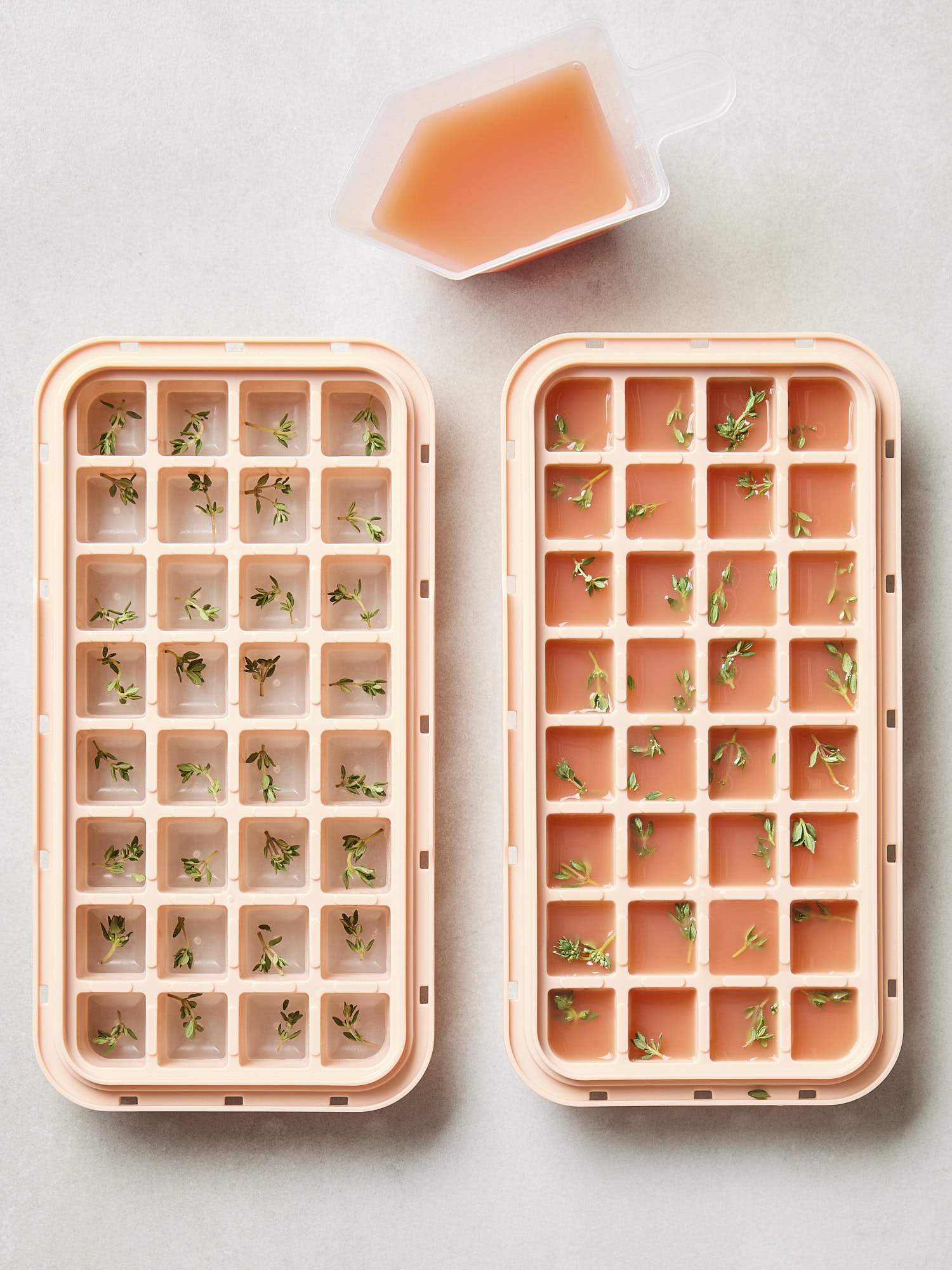 Two ice cube trays filled with fresh thyme and grapefruit juice.