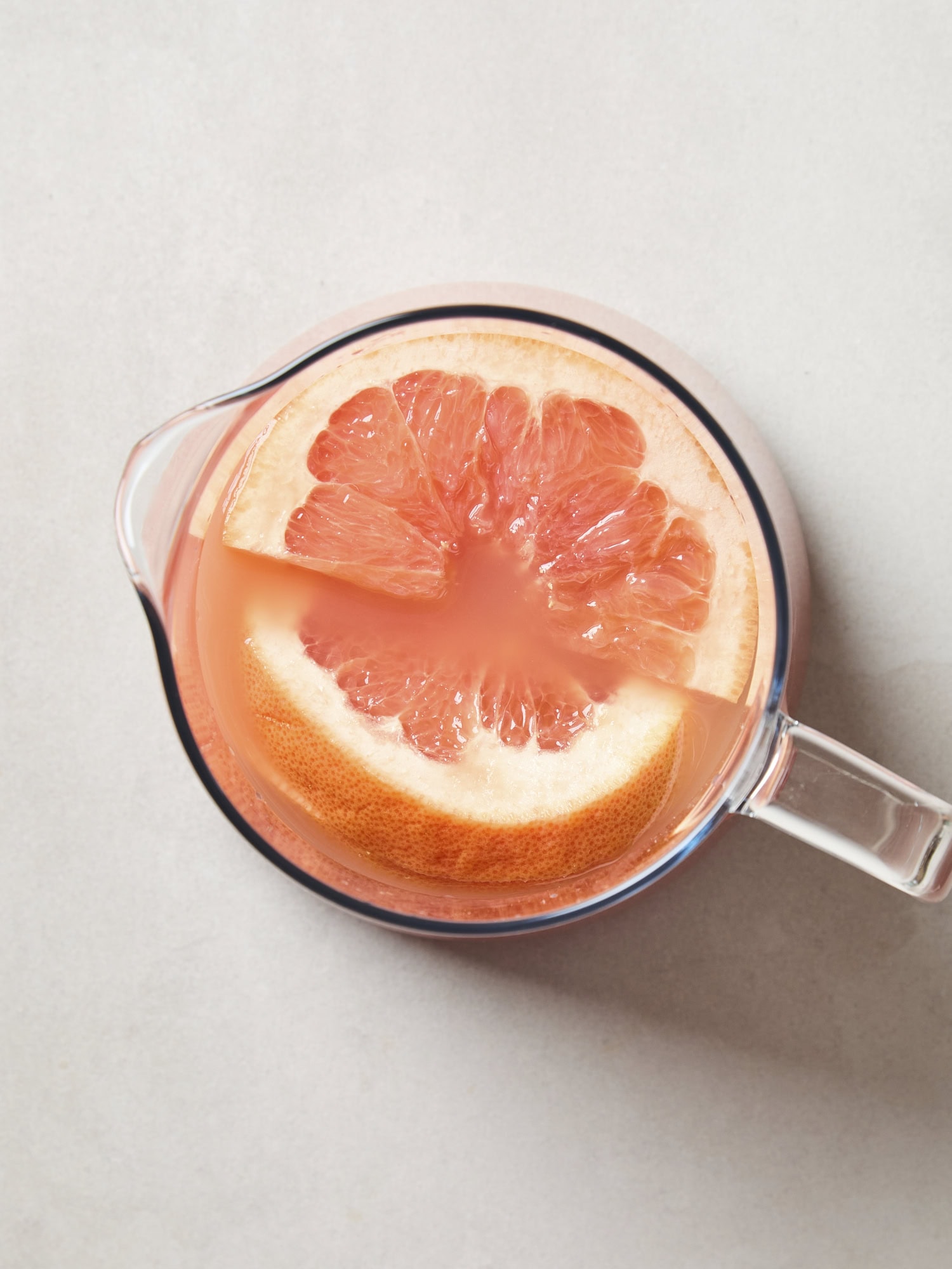 A glass pitcher filled with grapefruit juice with grapefruit slices on top.