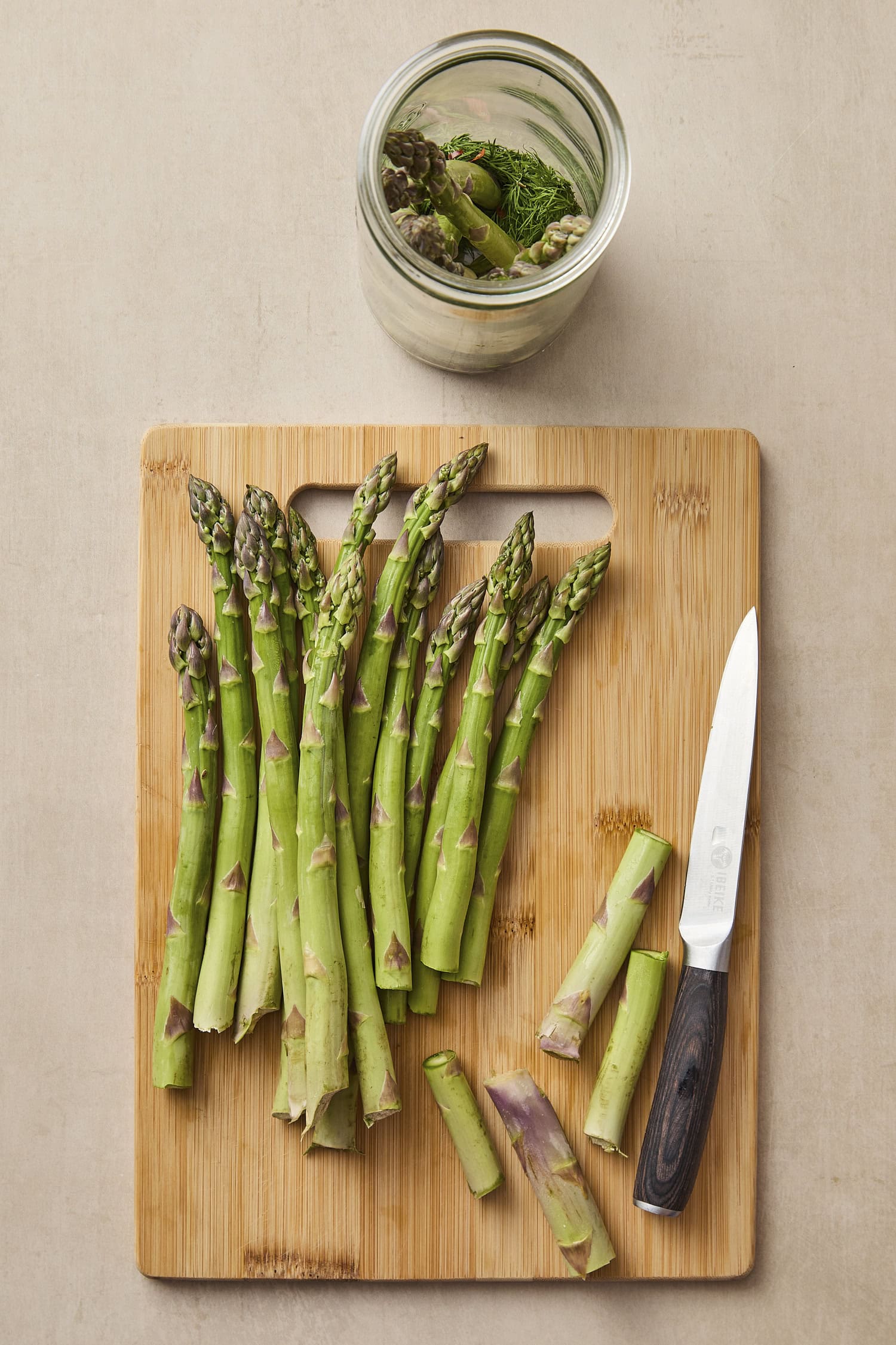 Cutting board with spears of asparagus being trimmed to equal length and being placed in a glass jar.