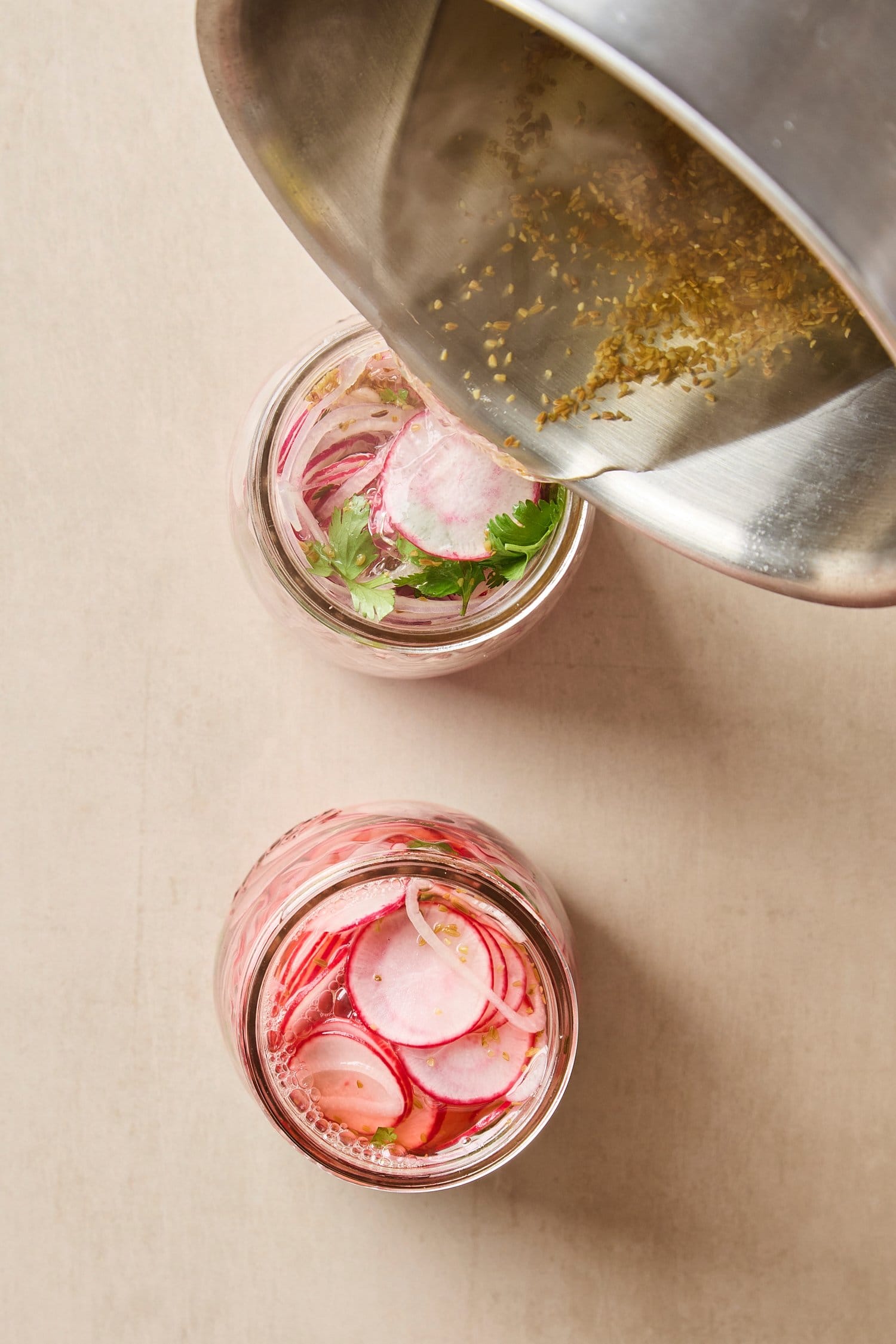 Saucepan pouring hot brine on top of sliced radishes in glass jars.
