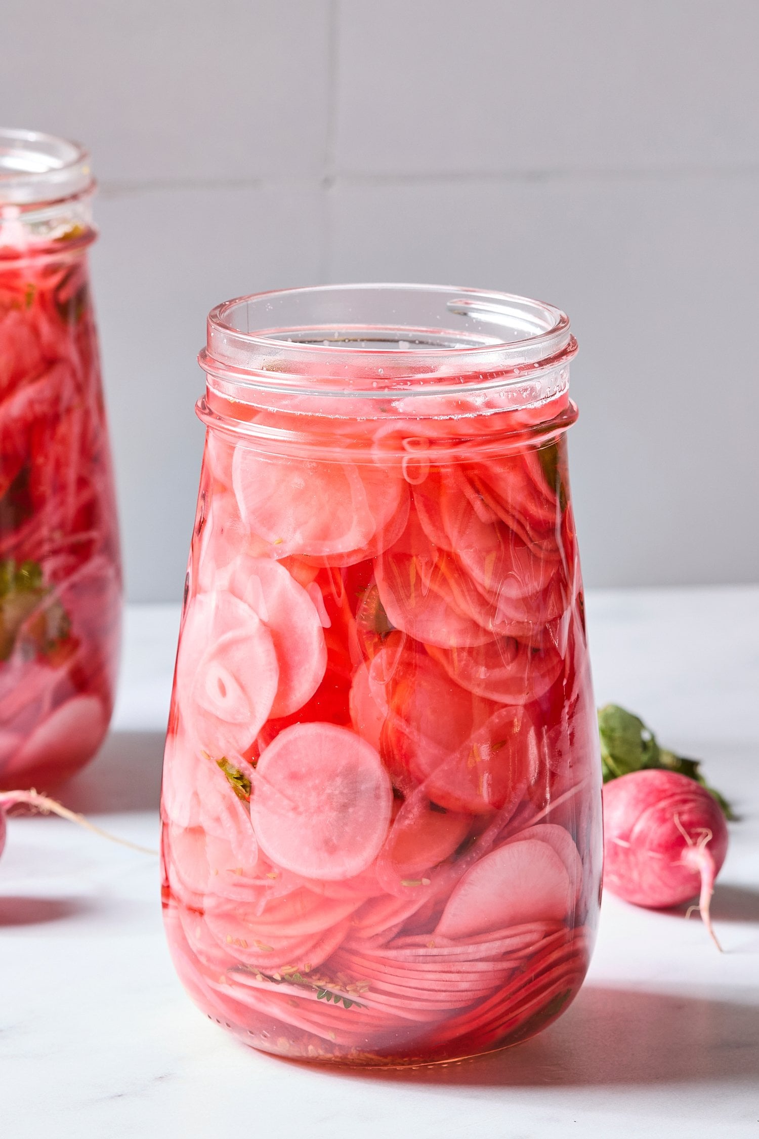 Glass jar filled with sliced radishes in pink liquid for pickling.