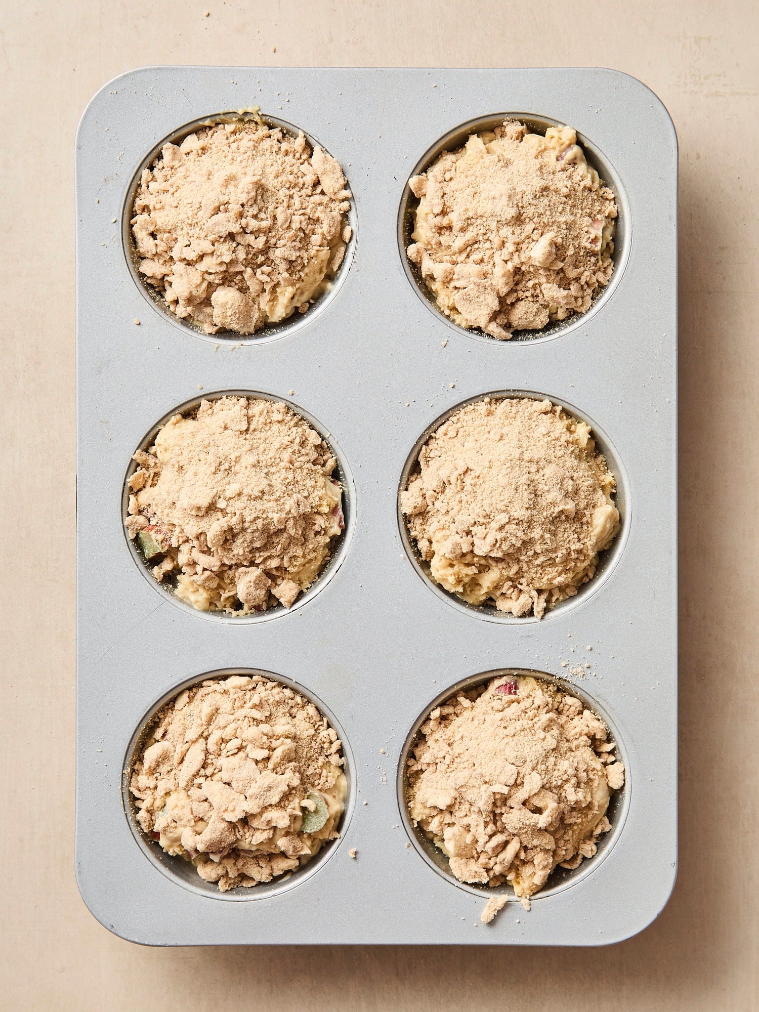 Muffin pan with unbaked muffins with streusel on top.