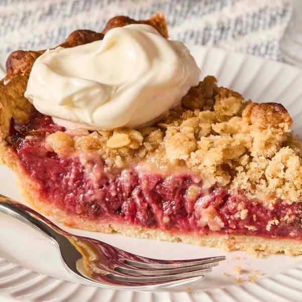 White plate with fork and slice of strawberry rhubarb pie with dollop of whipped cream.