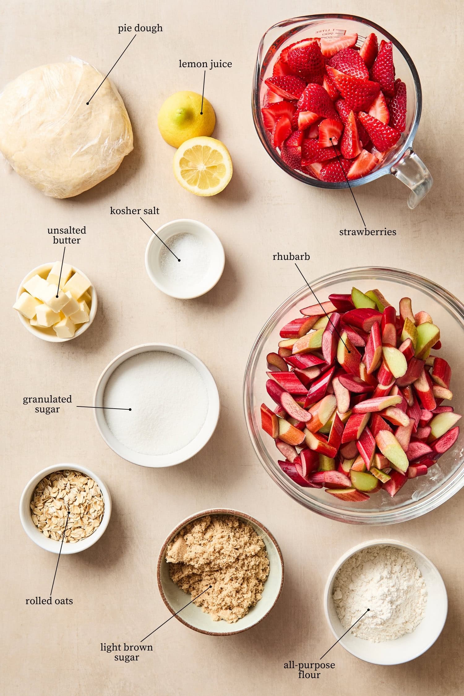 Surface with ingredients needed for a strawberry rhubarb pie including chopped rhubarb, strawberries, and more.