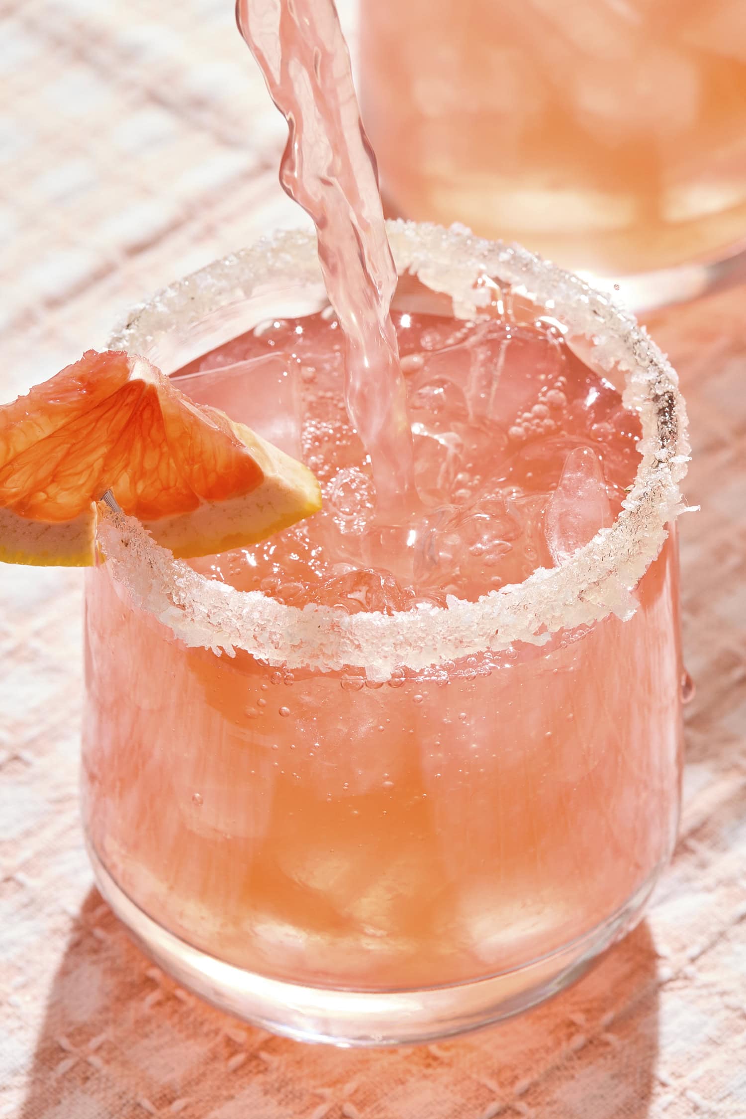 Pink liquid pouring into a cocktail glass filled with ice.