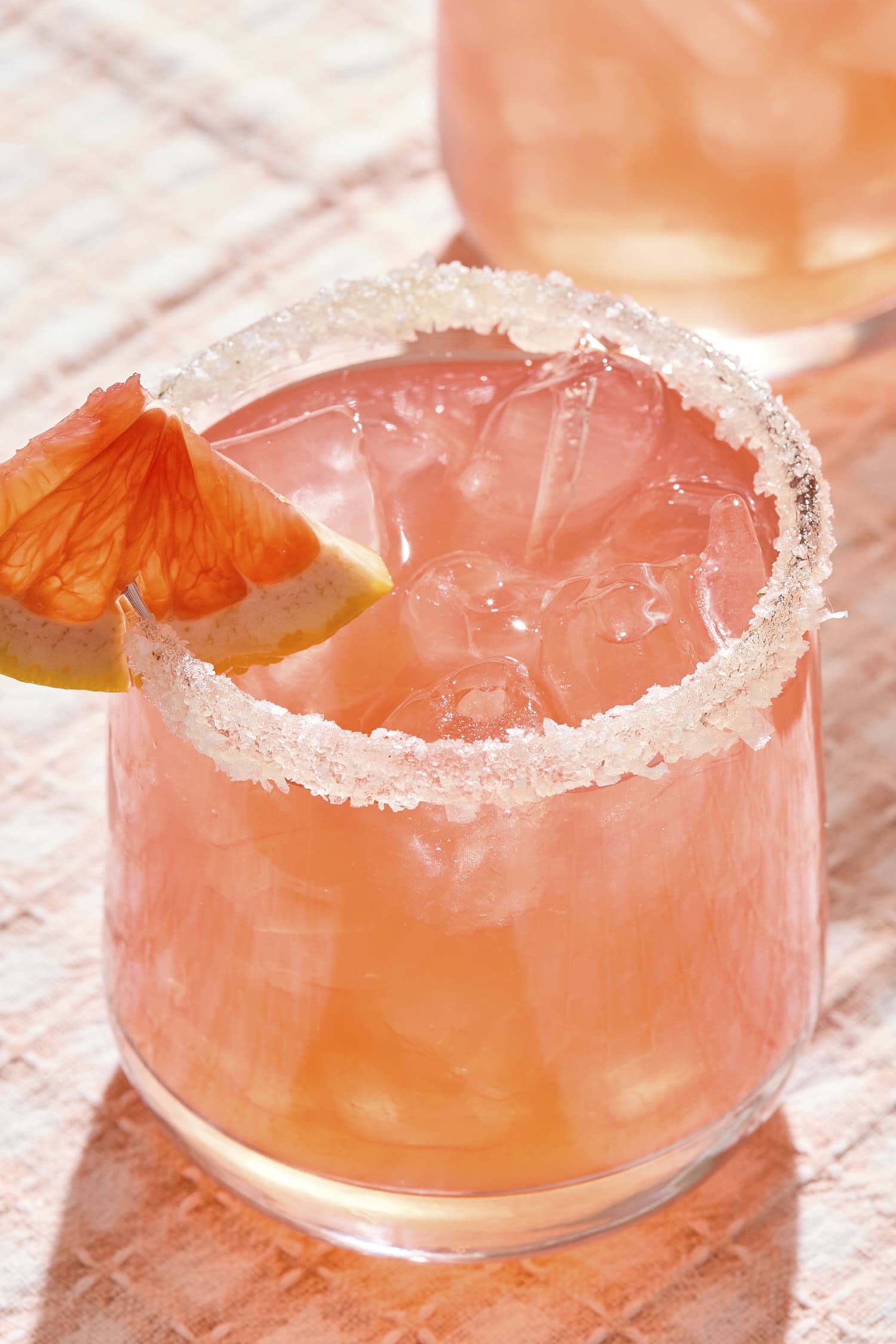 Salt-rimmed glass filled with pink-colored siesta cocktail with grapefruit wedge.