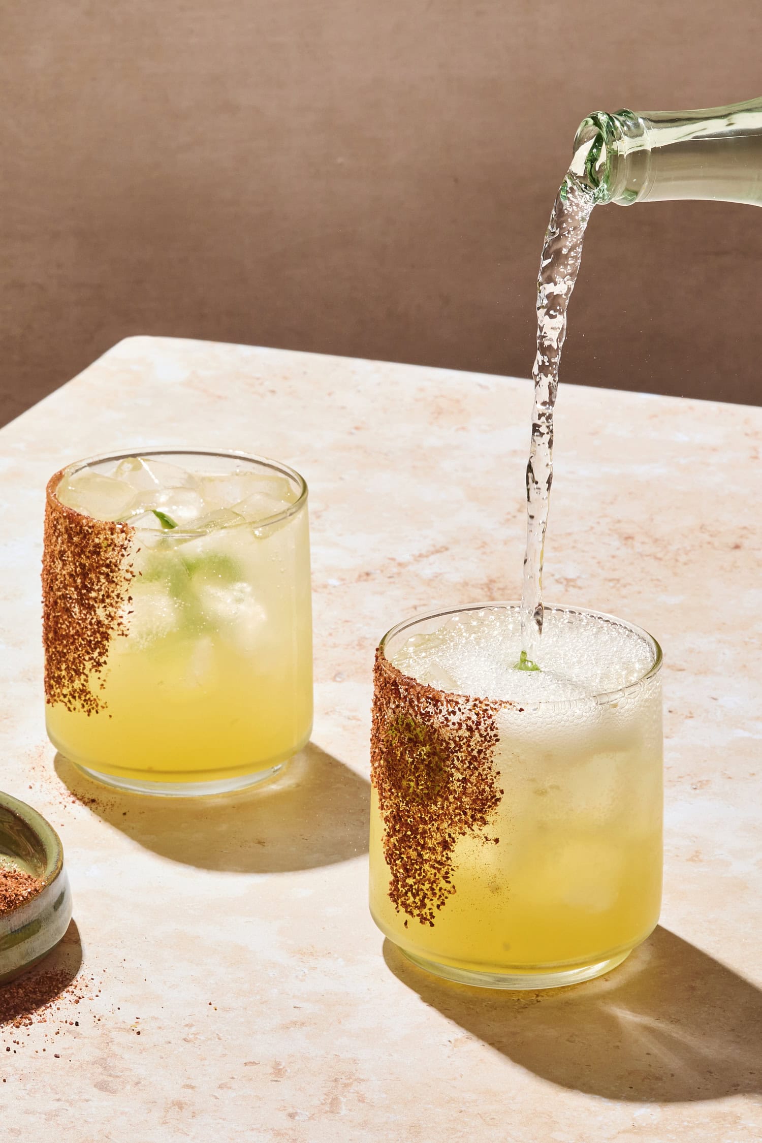 Sparkling water pouring into glass with margarita with salted rim.