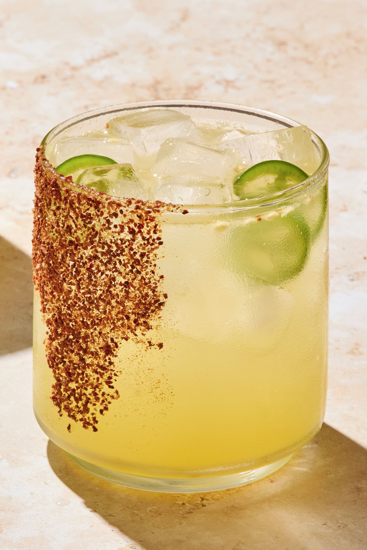 Glass with tajin on rim filled with spicy margarita with jalapenos in glass.