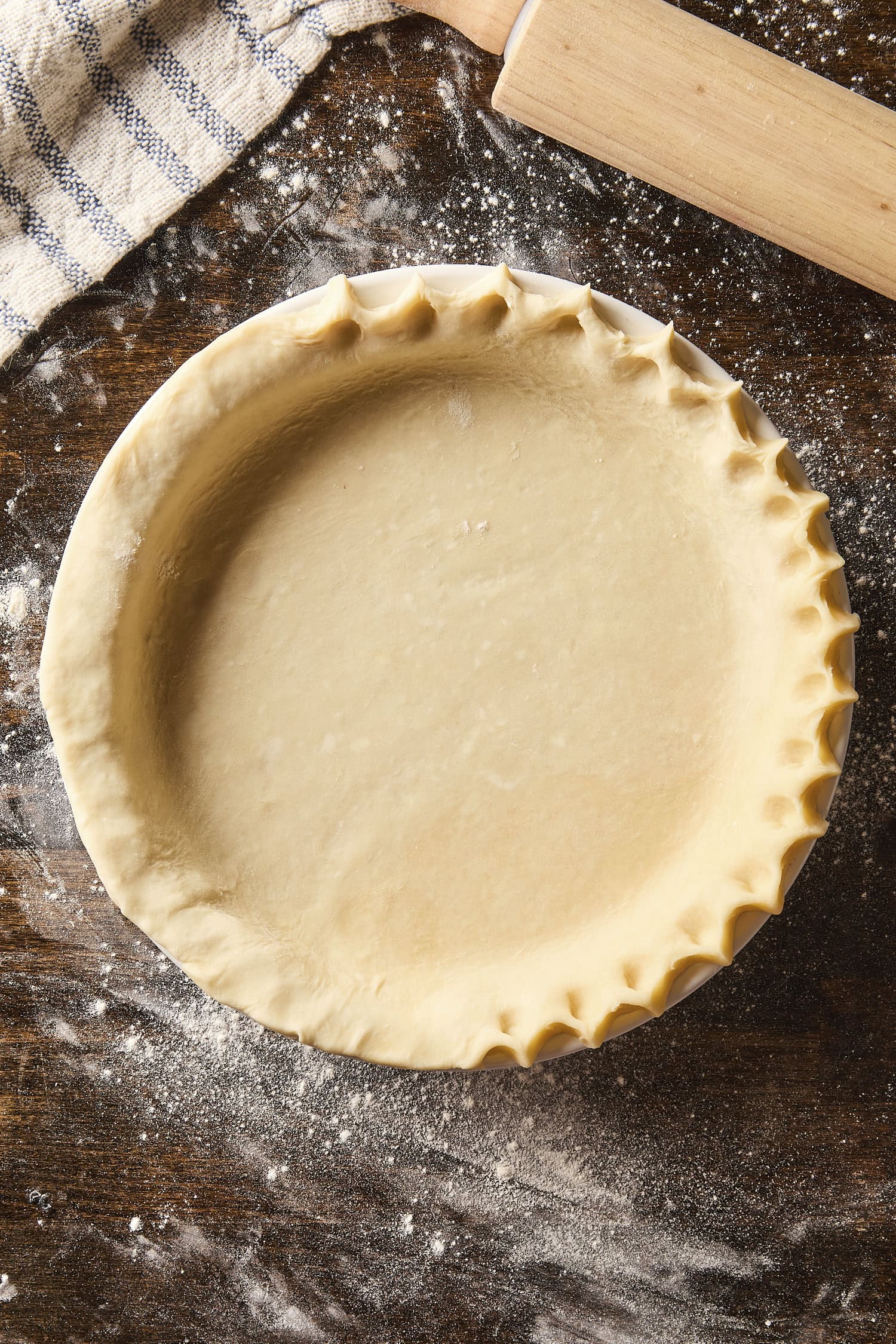 Pie crust in a baking dish with edges being crimped before being baked.