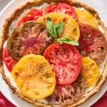 White plate with baked tomato tart on top with fresh basil garnish.