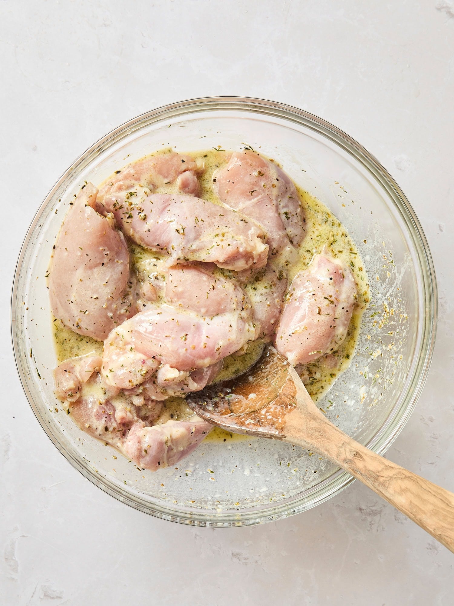 Glass bowl with marinating chicken thighs.