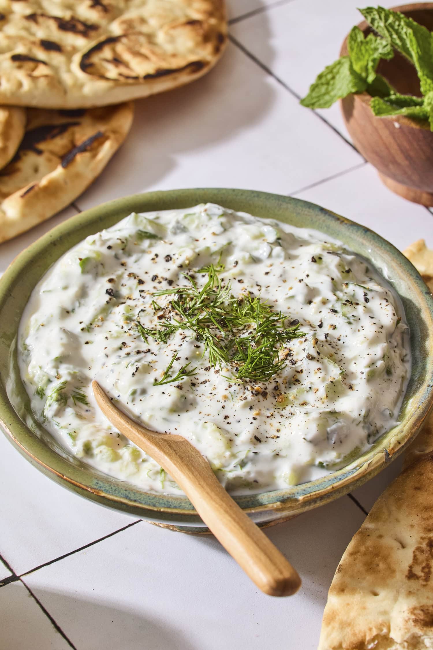 Green bowl filled with creamy tzatziki sauce with pita in background.