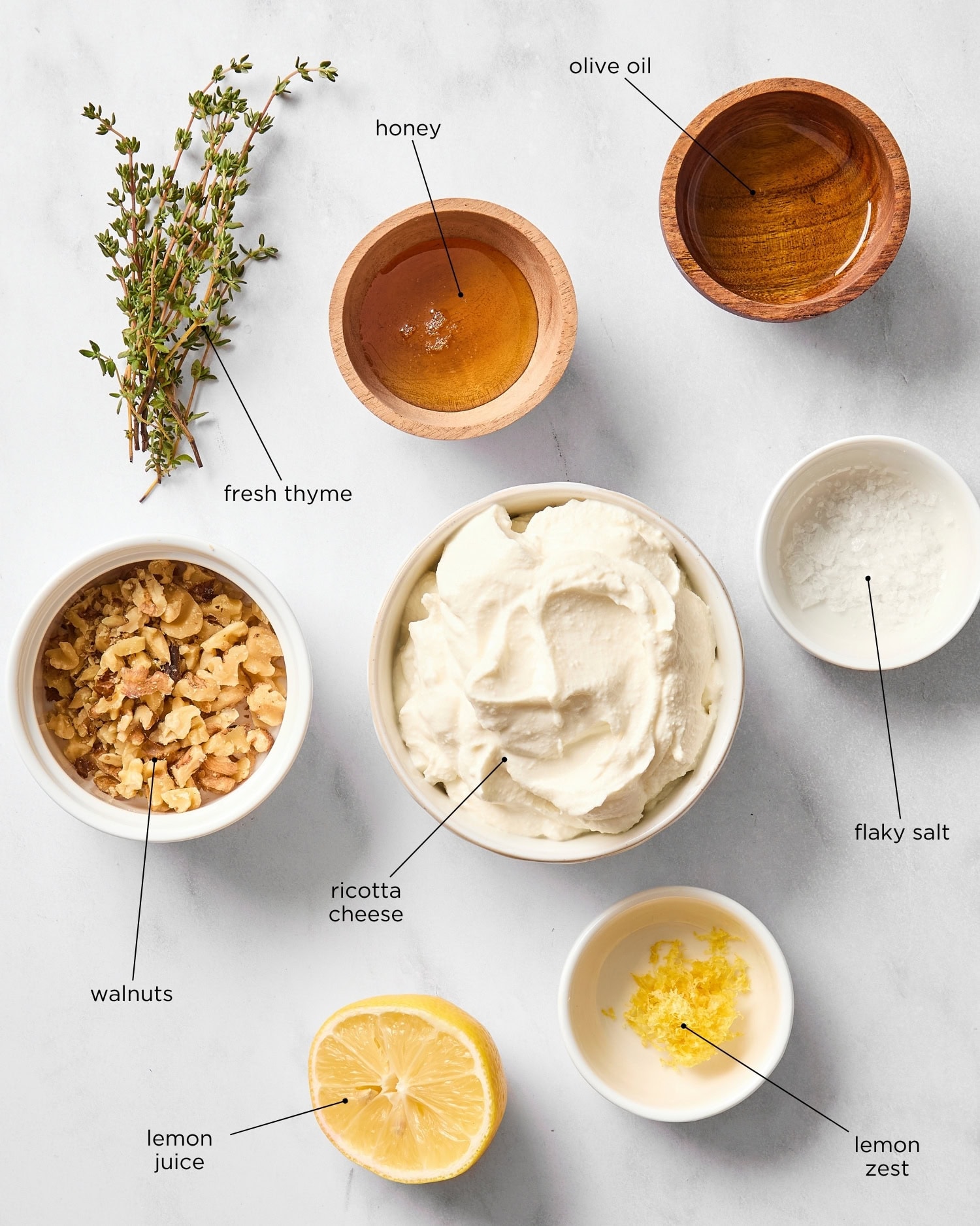 White marble surface with ingredients for whipped ricotta dip including walnuts, ricotta, lemon, and more.
