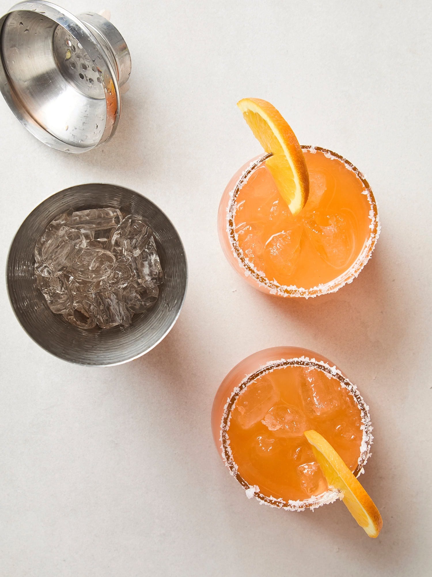 White surface with two Aperol margaritas from a cocktail shaker.