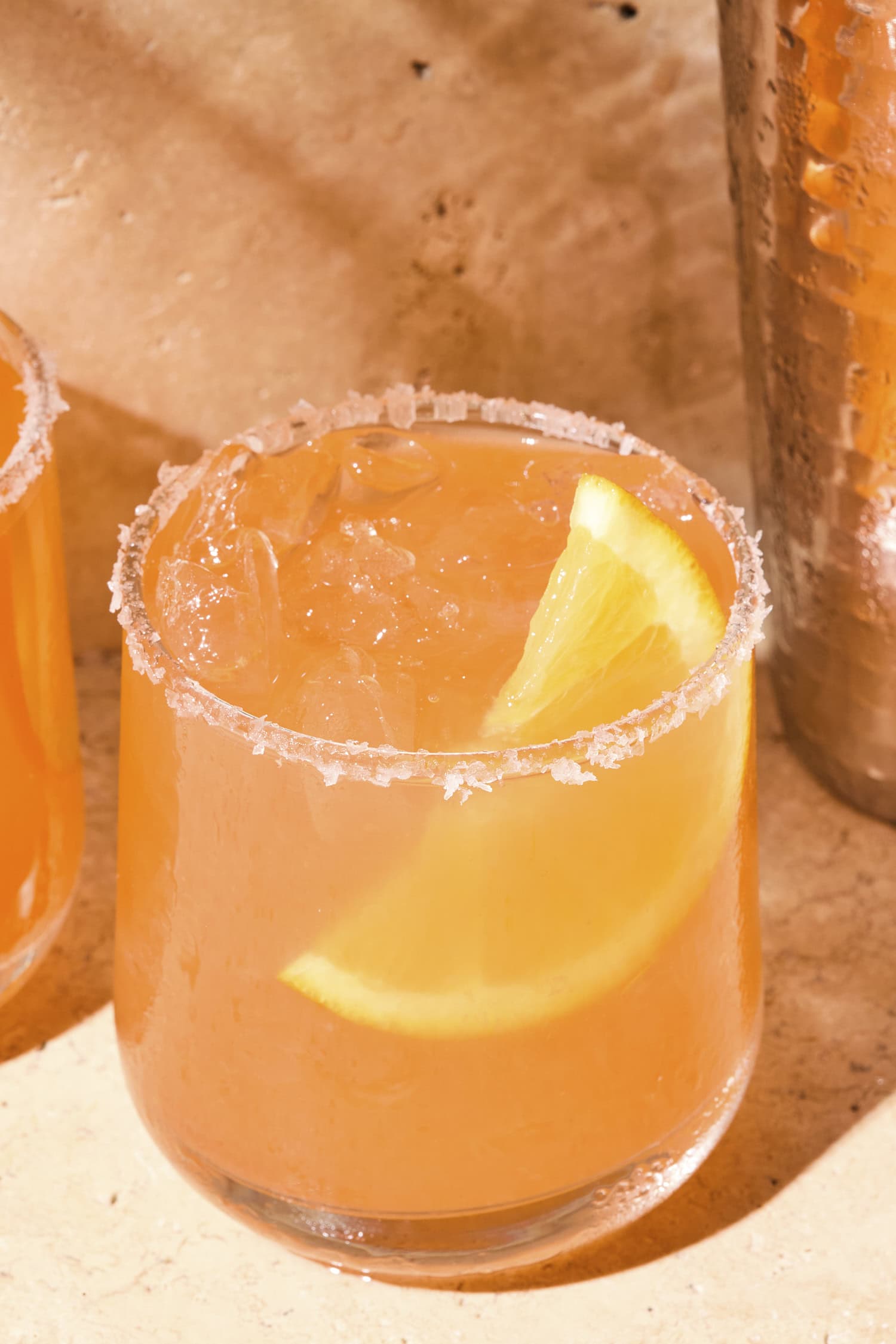 Aperol margarita drink with a flaky salt rim and an orange wedge in the drink.