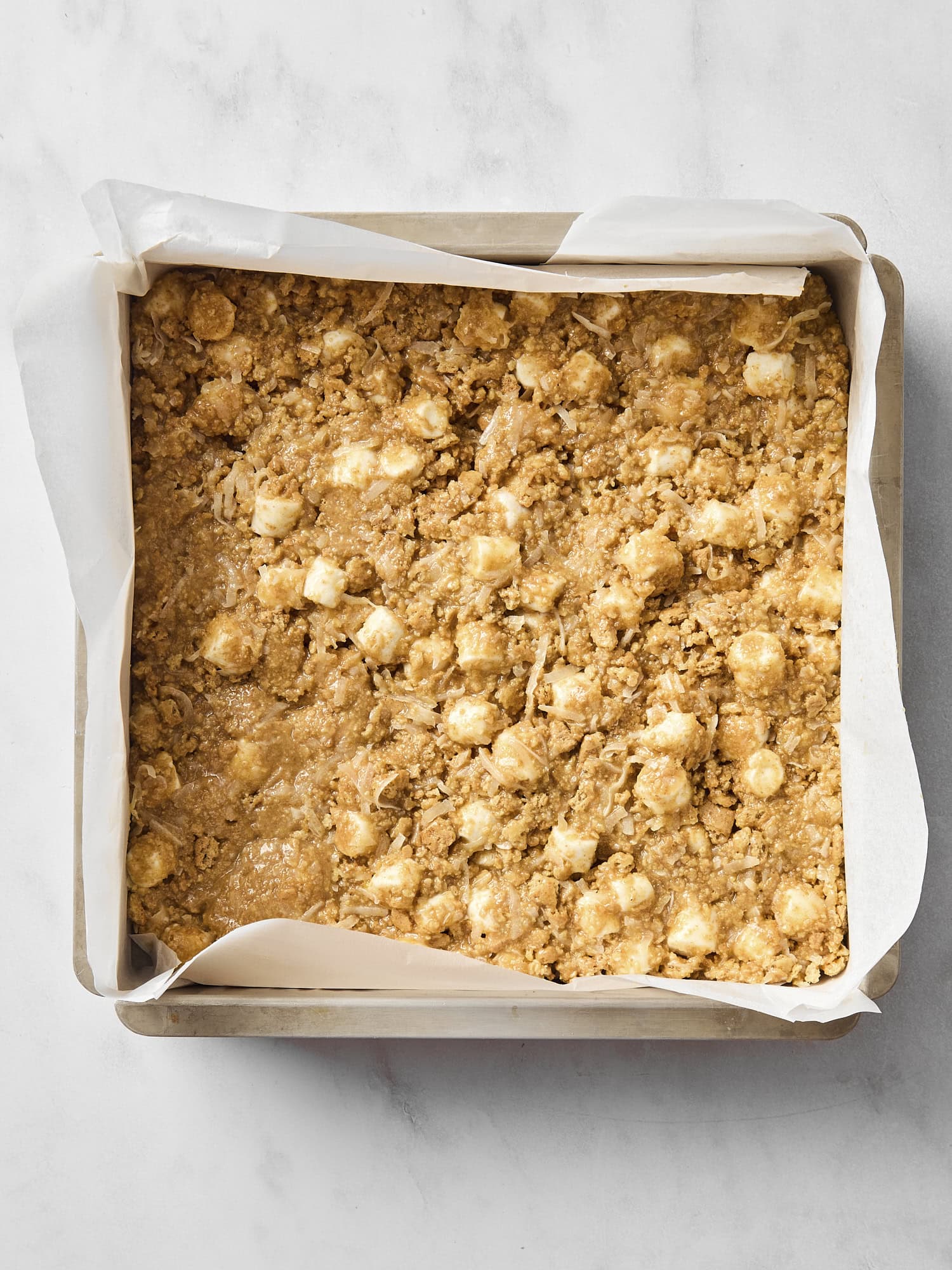 Baking pan with butterscotch bars pressed in with marshmallows and coconut flakes showing.