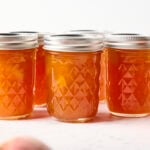 Jars of peach jam on a marble surface.