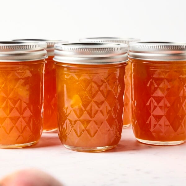 Jars of peach jam on a marble surface.