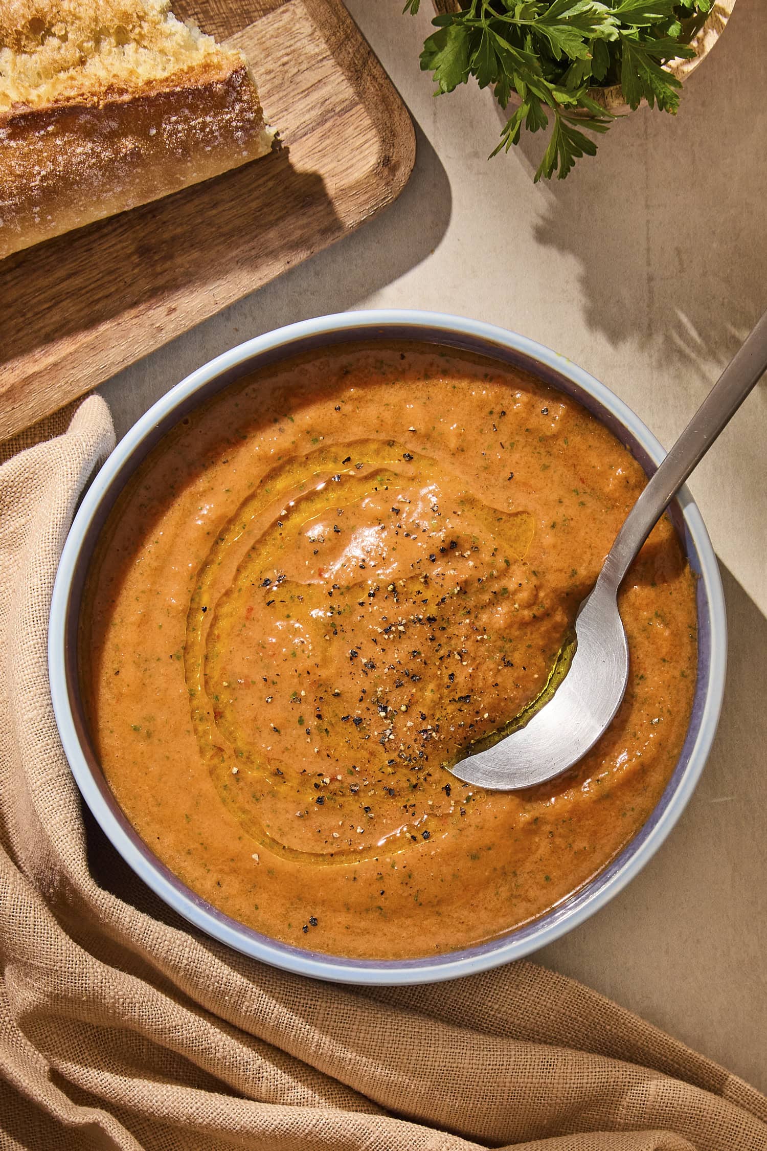 Bowl of creamy tomato-filled gazpacho soup with cutting board to the side.