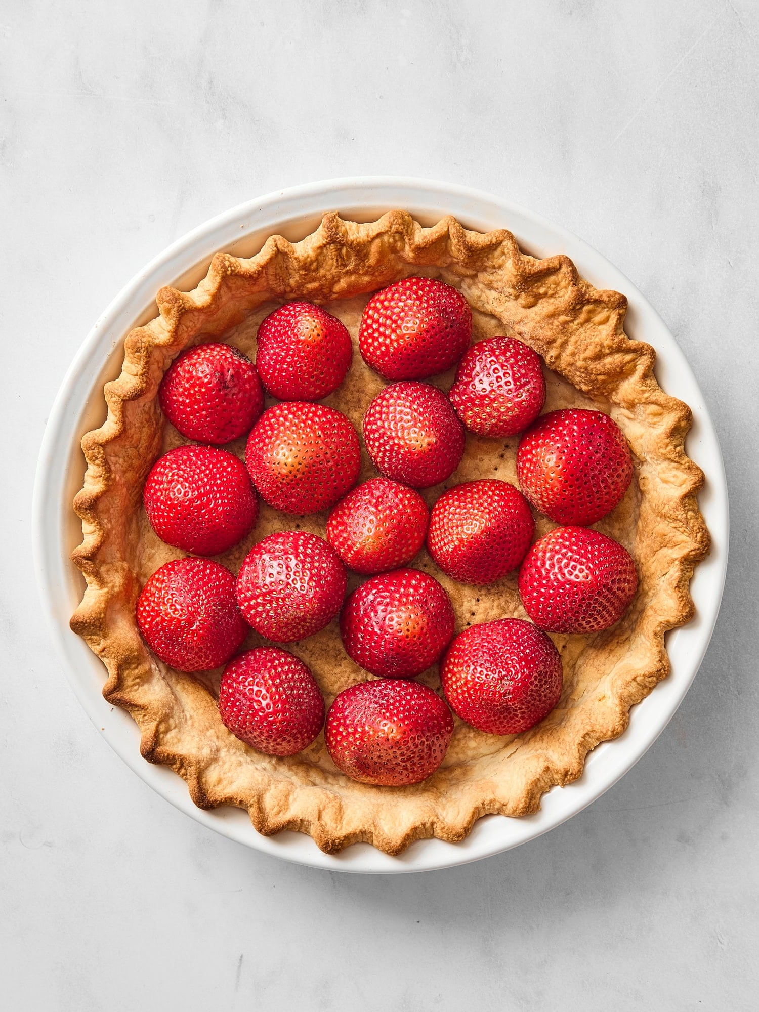 Baked crust for a pie with strawberries lined up inside.