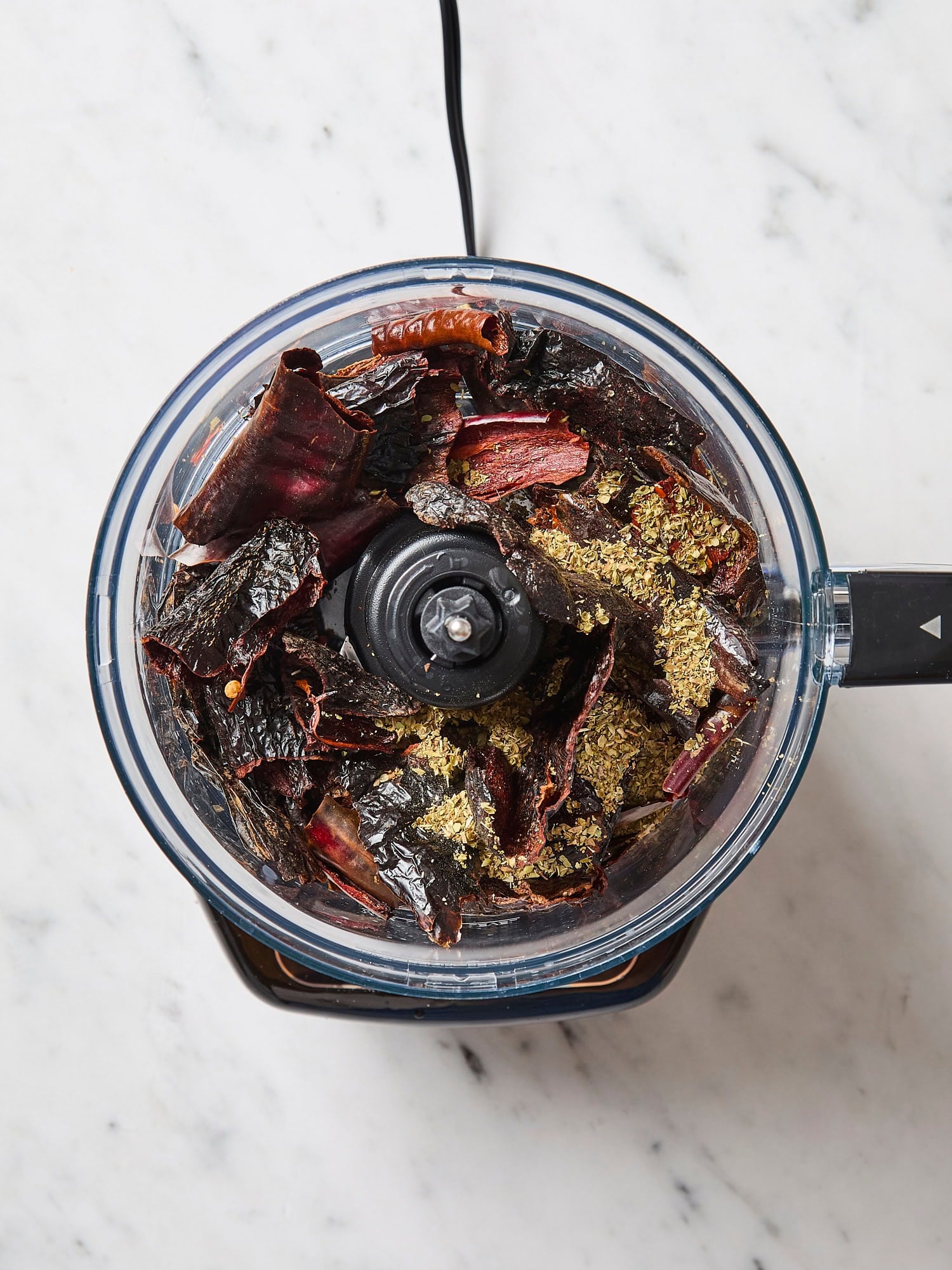 Food processor with cut up dried chiles before being ground up.