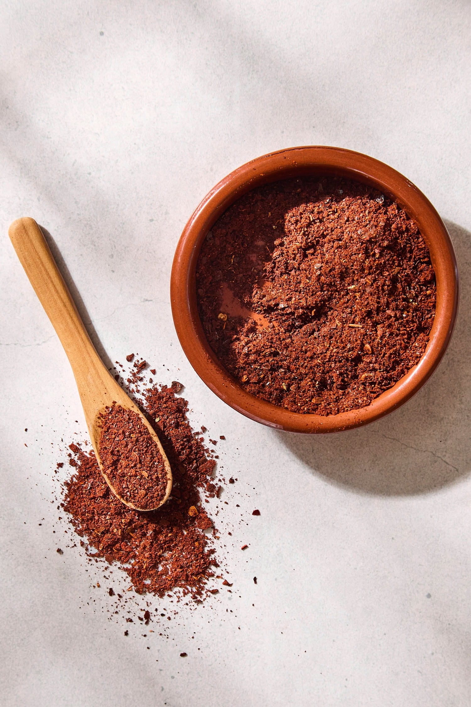 Brown bowl filled with homemade chili powder with a spoon scooping some.