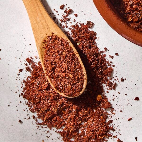 Concrete surface with homemade chili powder with reddish color on a spoon.