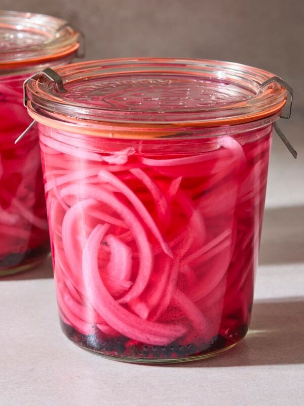 Jar filled with purple colored pickled red onions with lid on top.