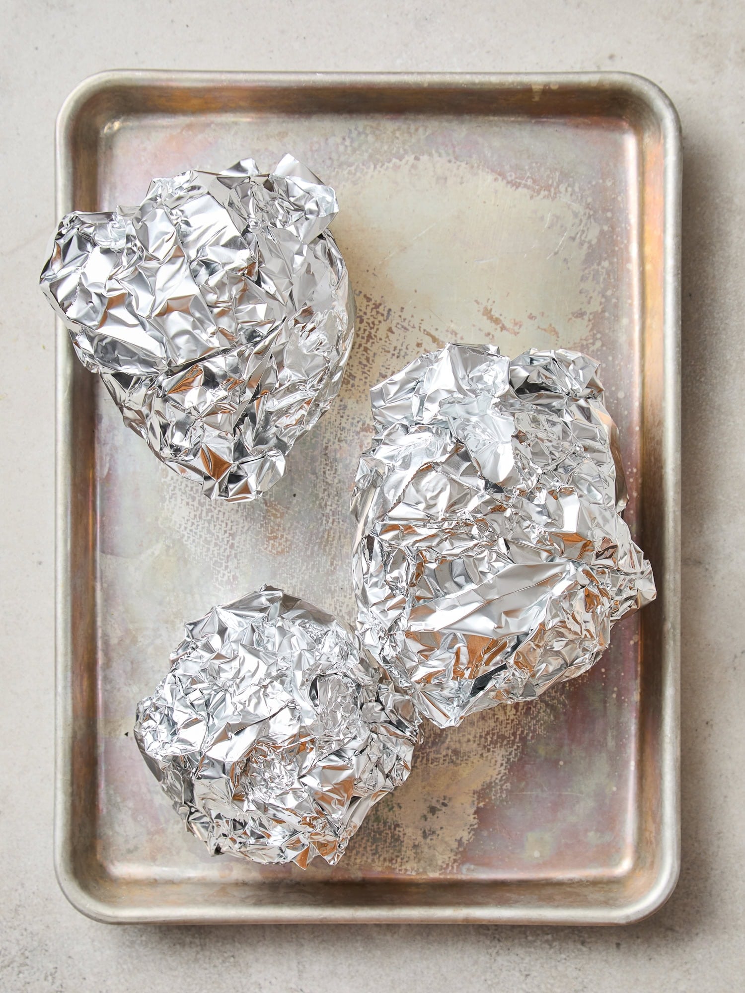 Beets wrapped in foil sit on a baking sheet prior to being cooked in the oven.