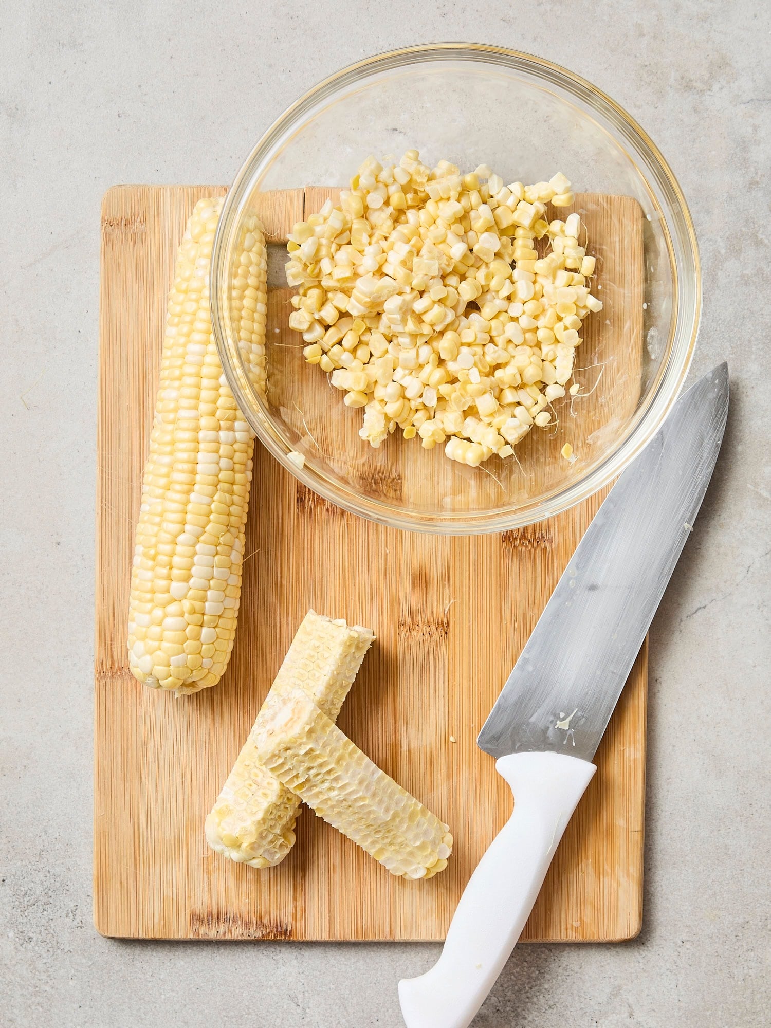 Cutting board slicing off kernels with one cob sliced in half.