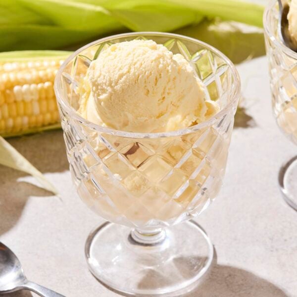 Glass container filled with a serving of ice cream with sweet corn ears in the background.