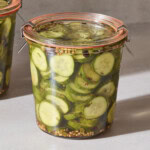 Two jars of sweet pickles with pickling spices in brine.