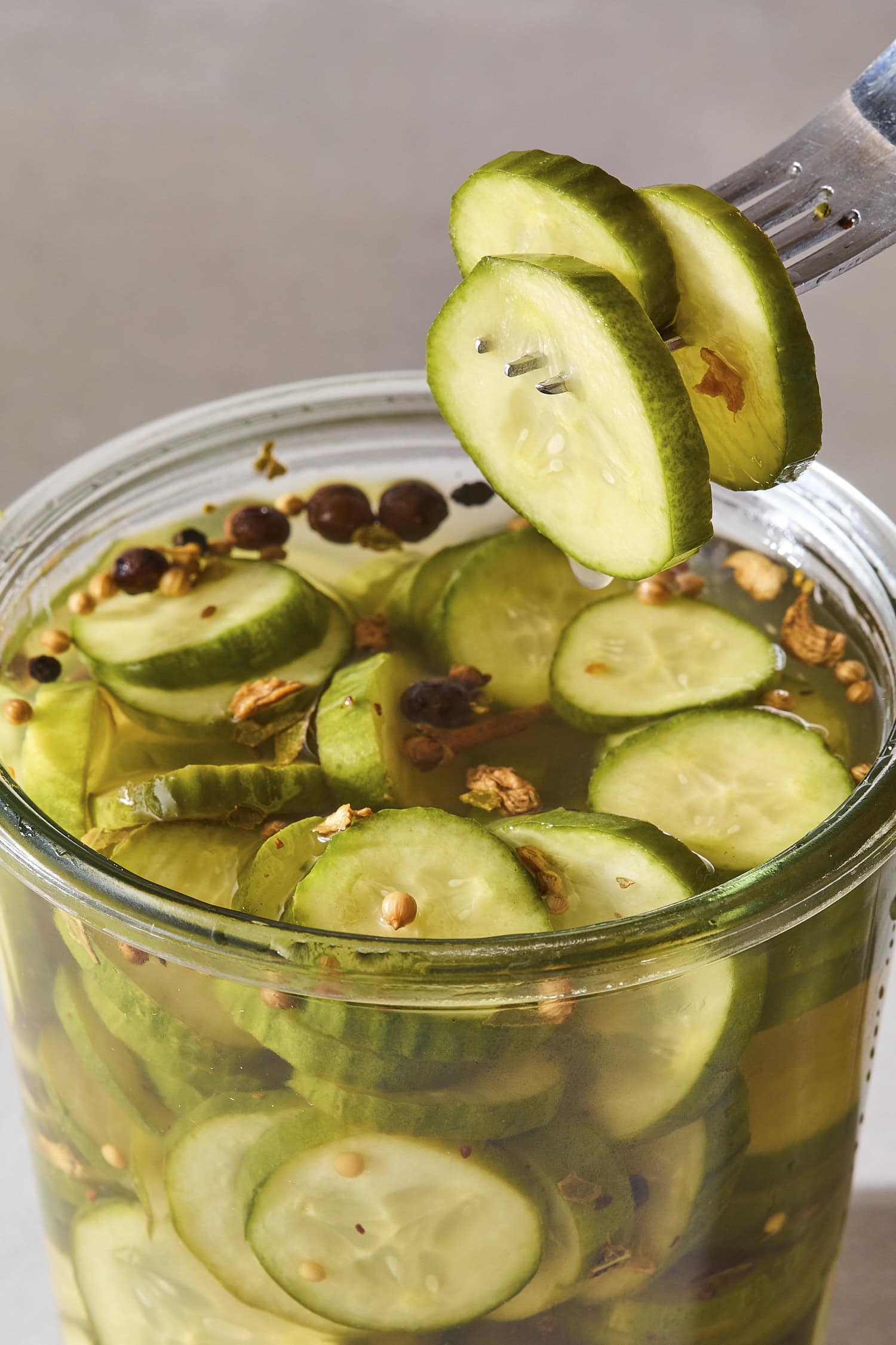 Fork spearing three sweet pickles from a jar filled with more pickles.