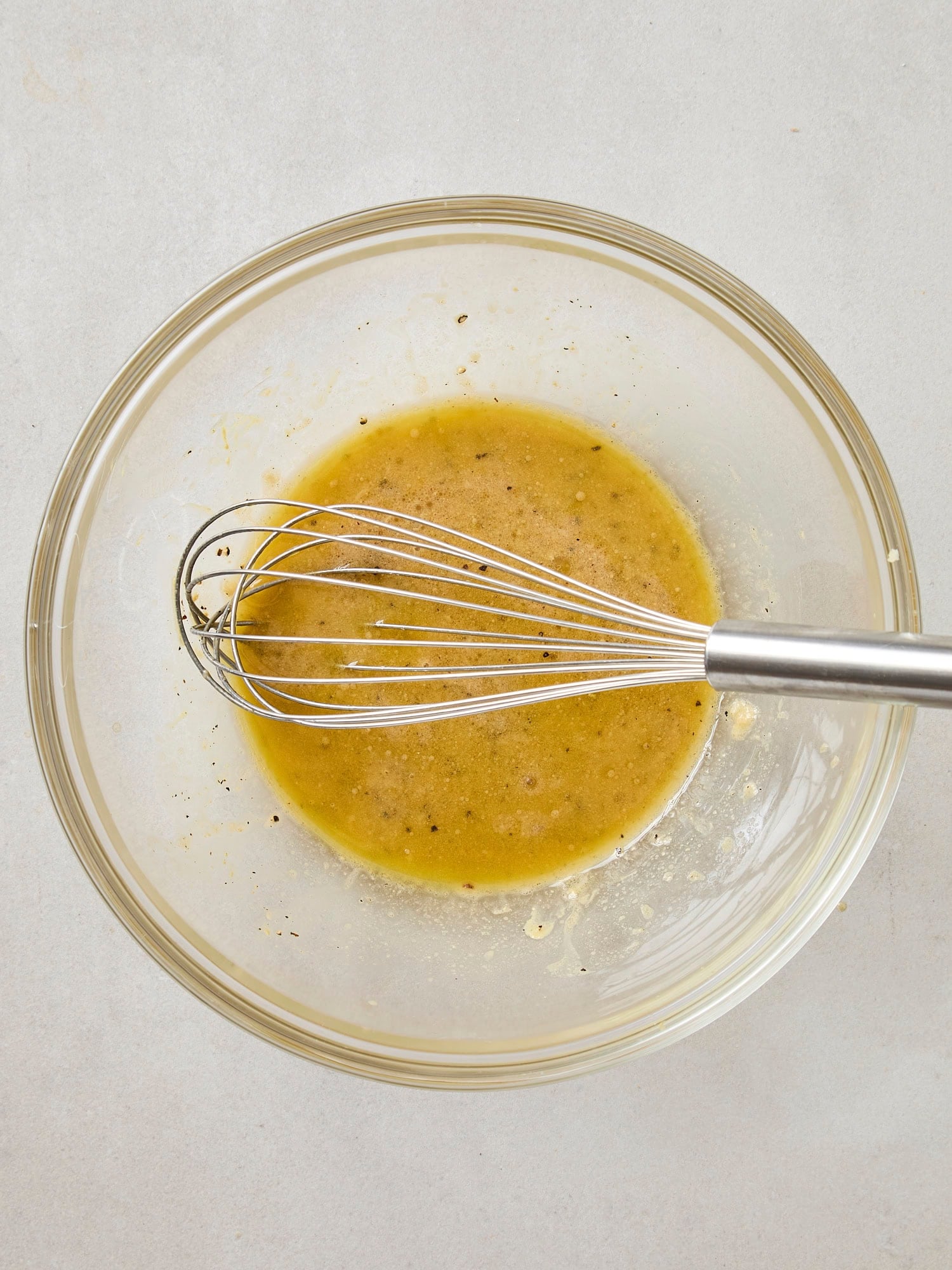 Bowl with a dressing being mixed together with a whisk in a glass bowl.