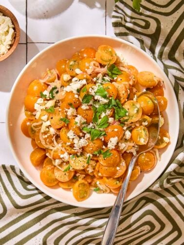 White serving bowl with tomato salad made with Sungold tomatoes and feta on top.