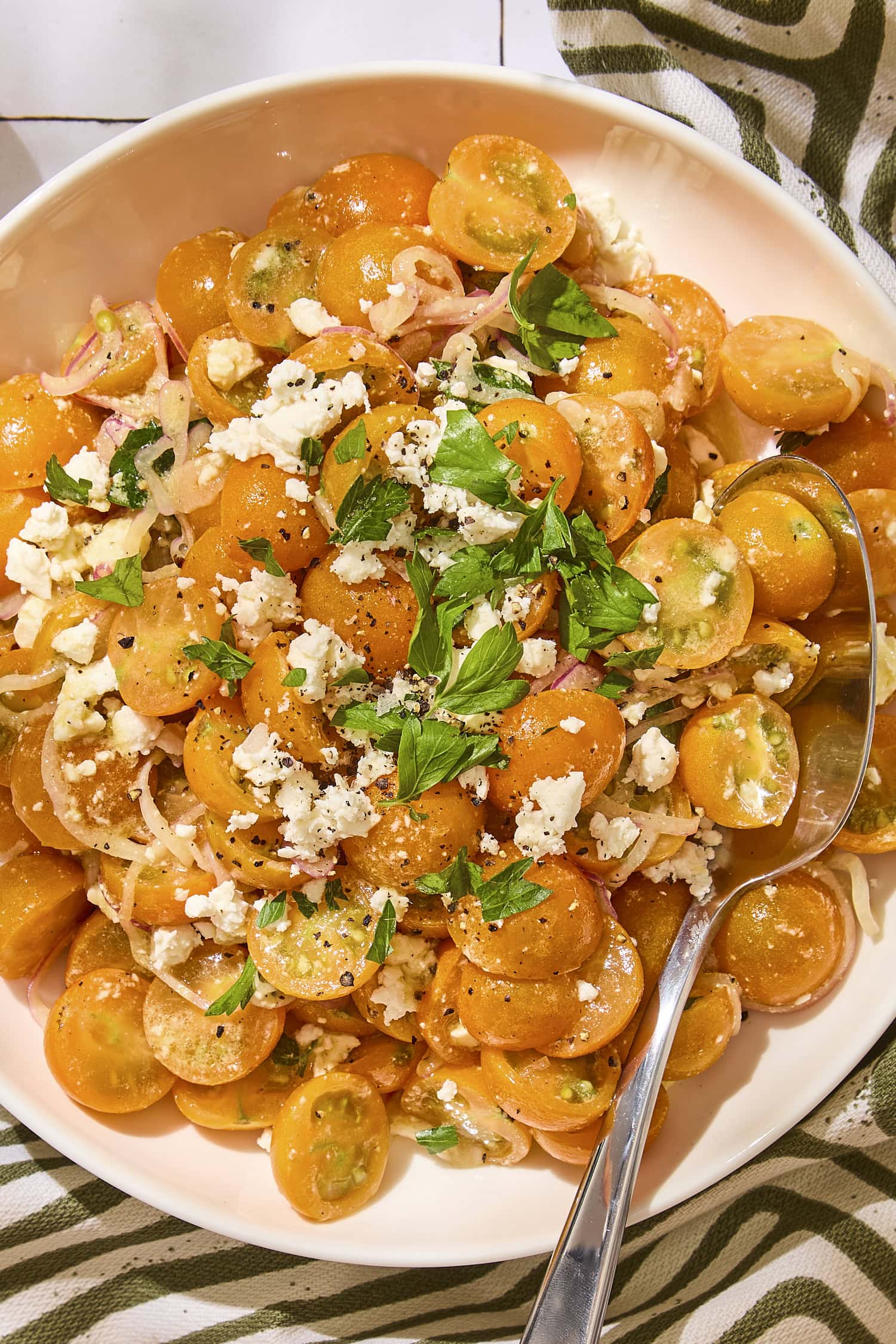 Cherry tomatoes sliced in half in a bowl topped with fresh parsley and feta cheese.