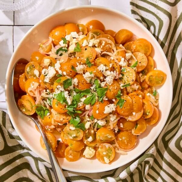 Bowl with yellow cherry tomatoes topped with feta cheese and parsley for a quick tomato salad.