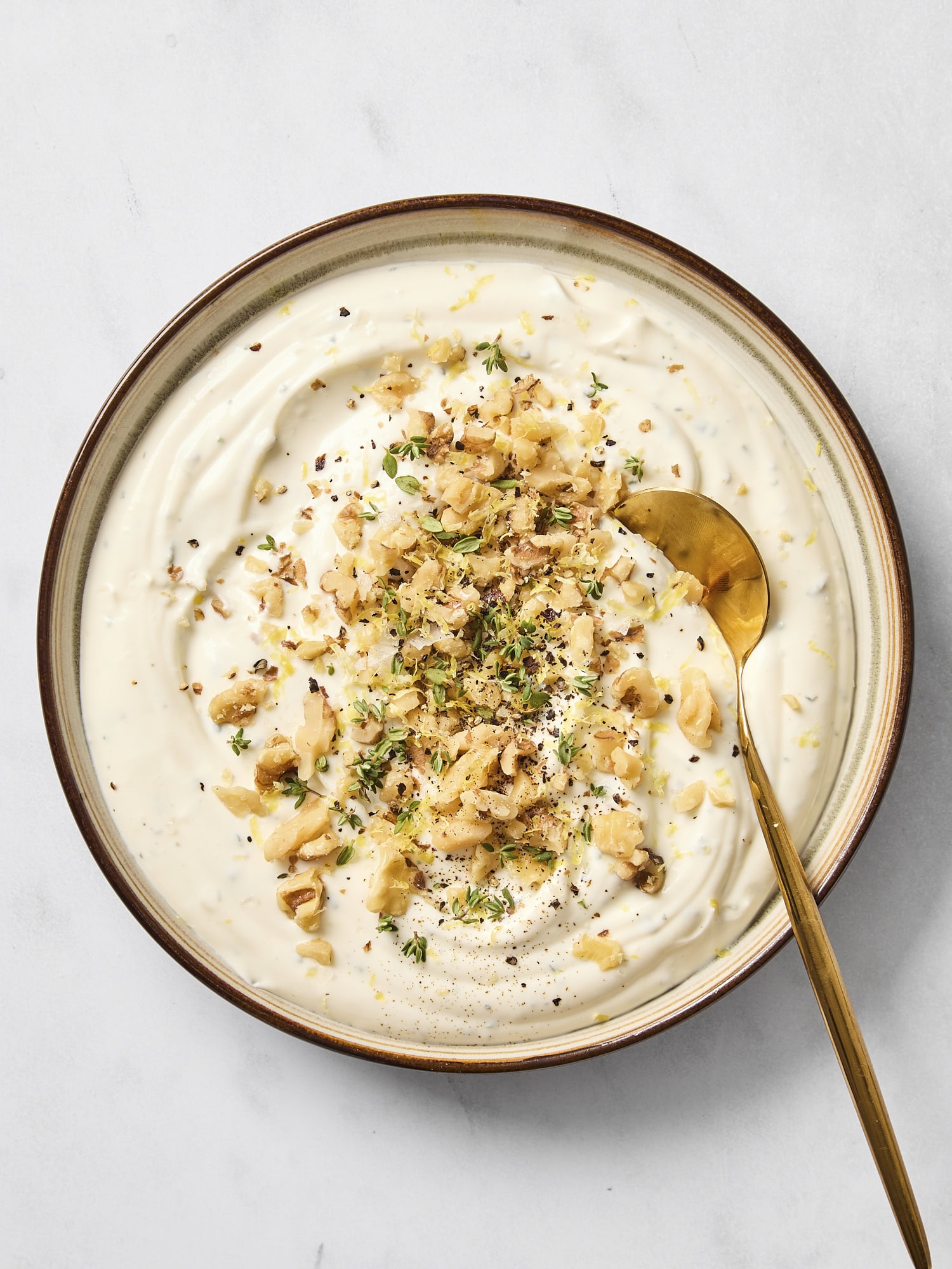 Brown bowl filled with freshly-made whipped ricotta dip topped with chopped walnuts and herbs.