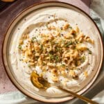 Bowl with ricotta dip topped with walnuts and herbs with spoon scooping.