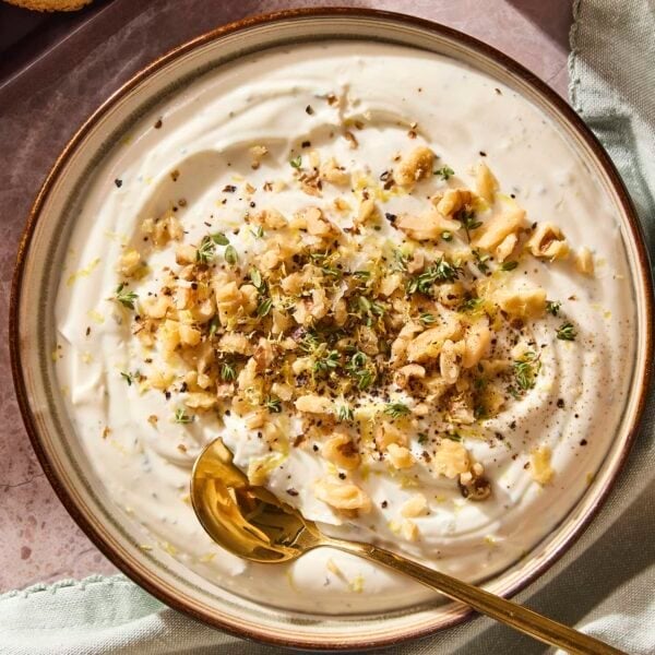 Bowl with ricotta dip topped with walnuts and herbs with spoon scooping.