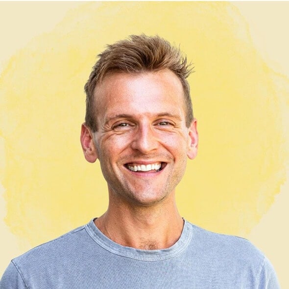 Kaleb Wyse wearing a blue shirt standing in front of a yellow background.
